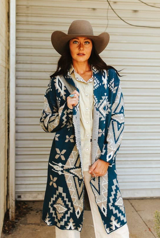 Woman wearing a blue patterned coat and cowboy hat in front of a white door.