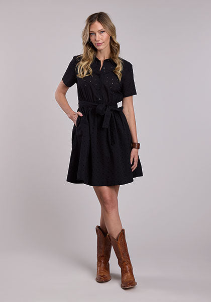 Woman wearing a black Stetson cotton eyelet Western shirt dress with short sleeves, button front, elastic waist, tie belt, and cowboy boots.