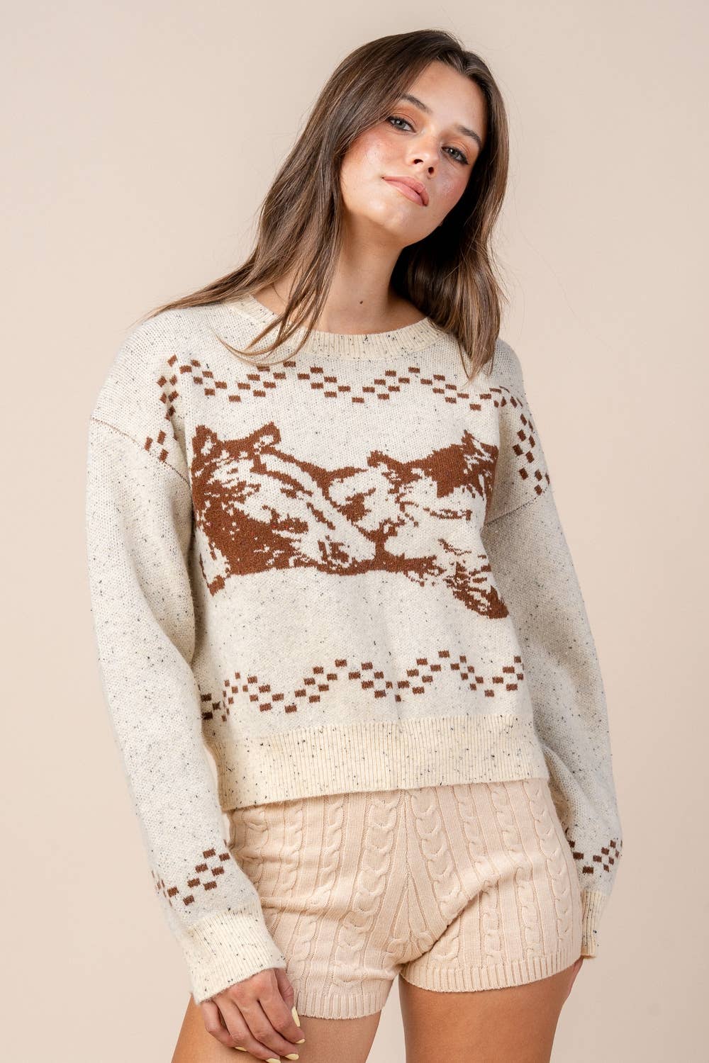 Woman wearing a patterned sweater and shorts against a beige background