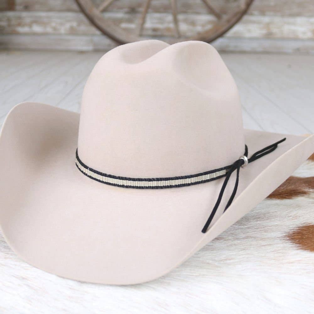 Beige cowboy hat with a black band on a wooden surface