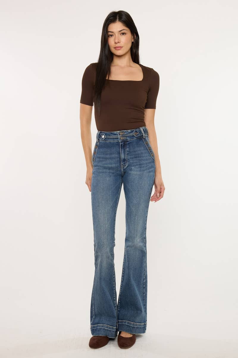 Woman wearing blue flared jeans and a brown top on a white background