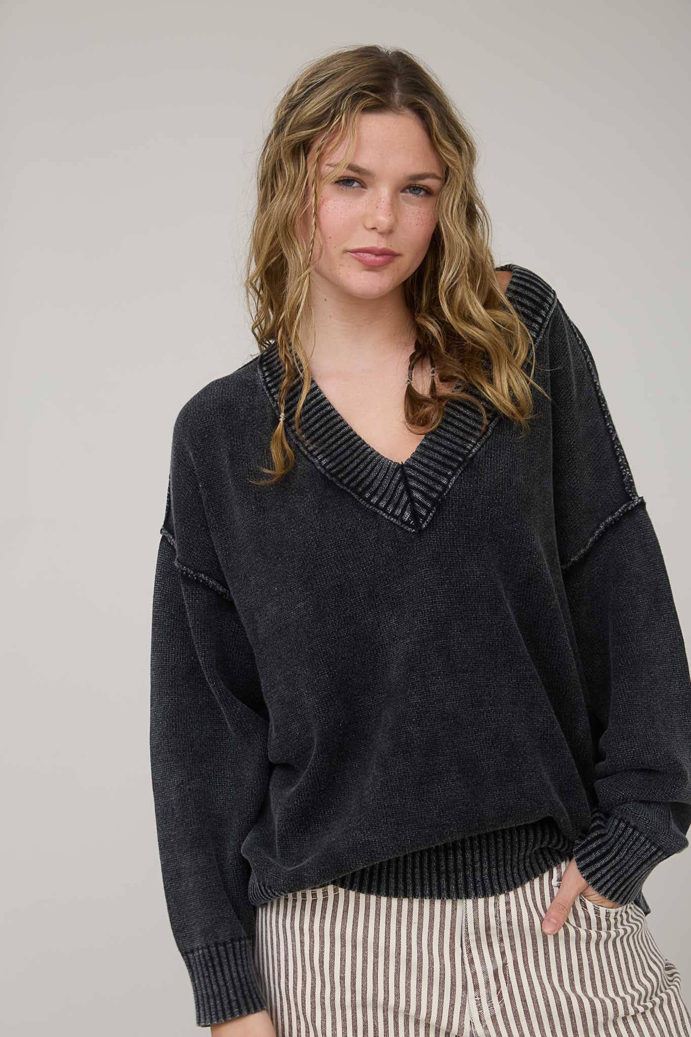 Woman wearing a dark sweater with a V-neckline against a plain background