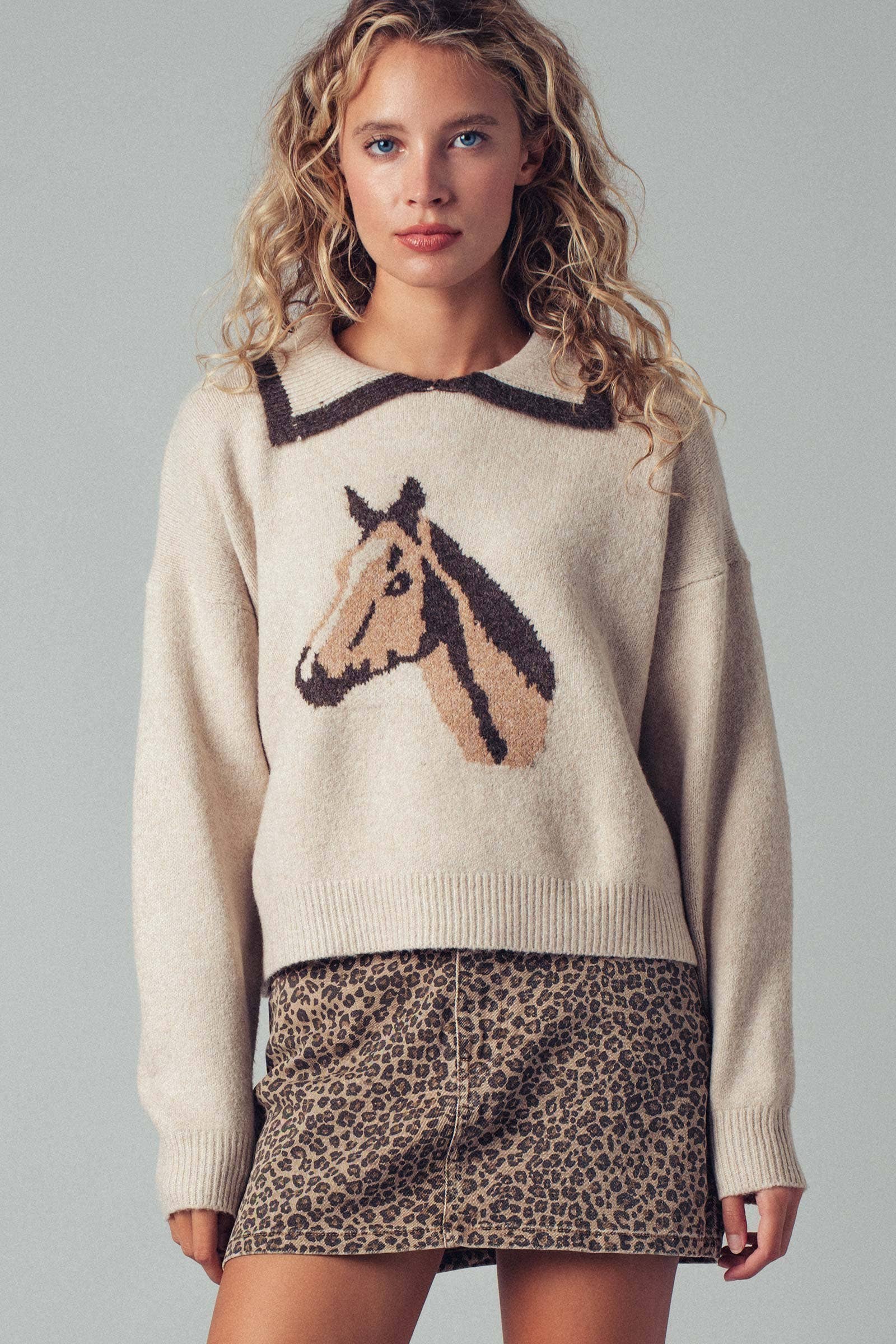 Woman wearing a sweater with a horse design and a leopard print skirt on a gray background