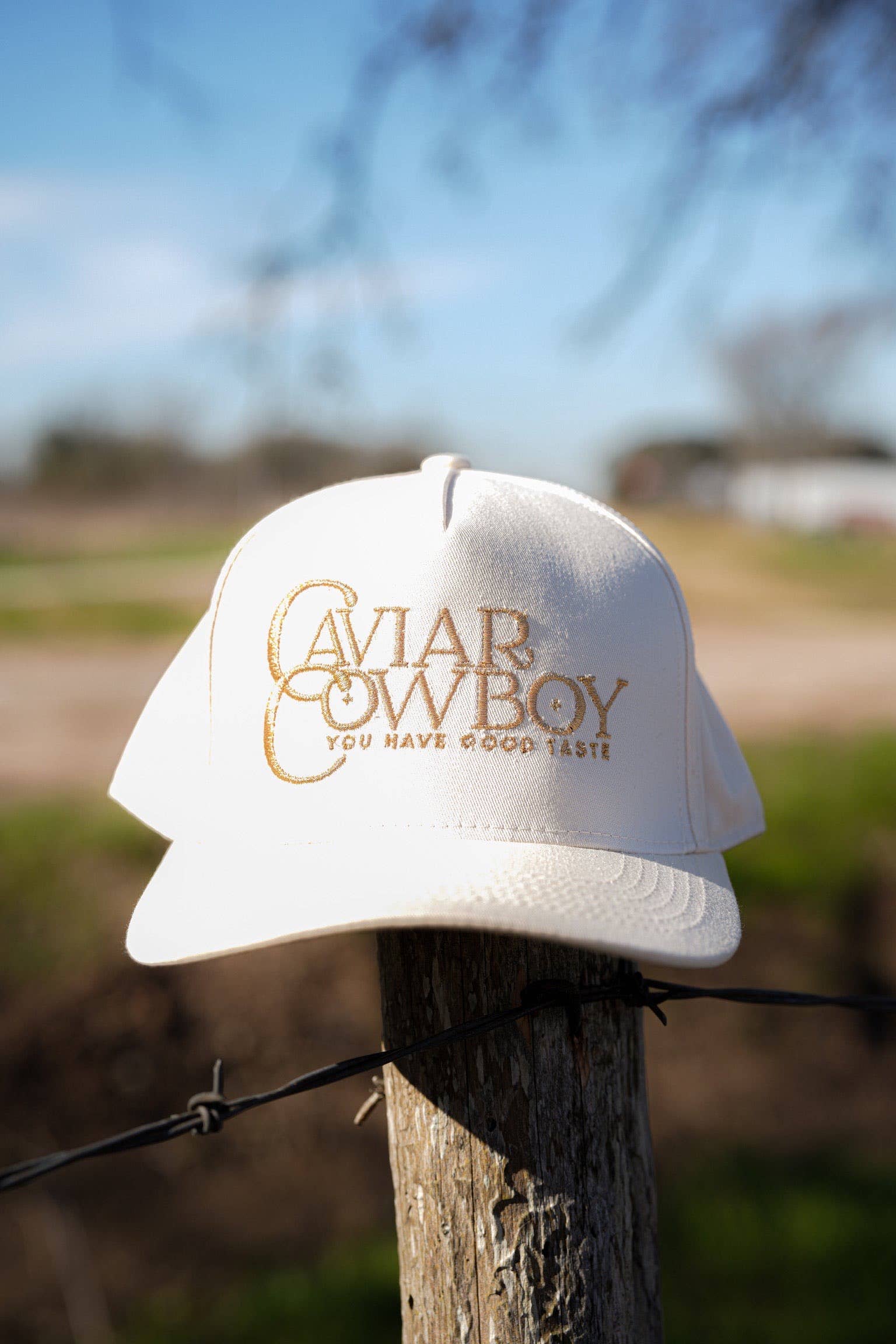 A cream-colored trucker hat with gold embroidered "Caviar Cowboy" lettering and "You Have Good Taste" slogan. A stylish blend of Western and luxury aesthetics.