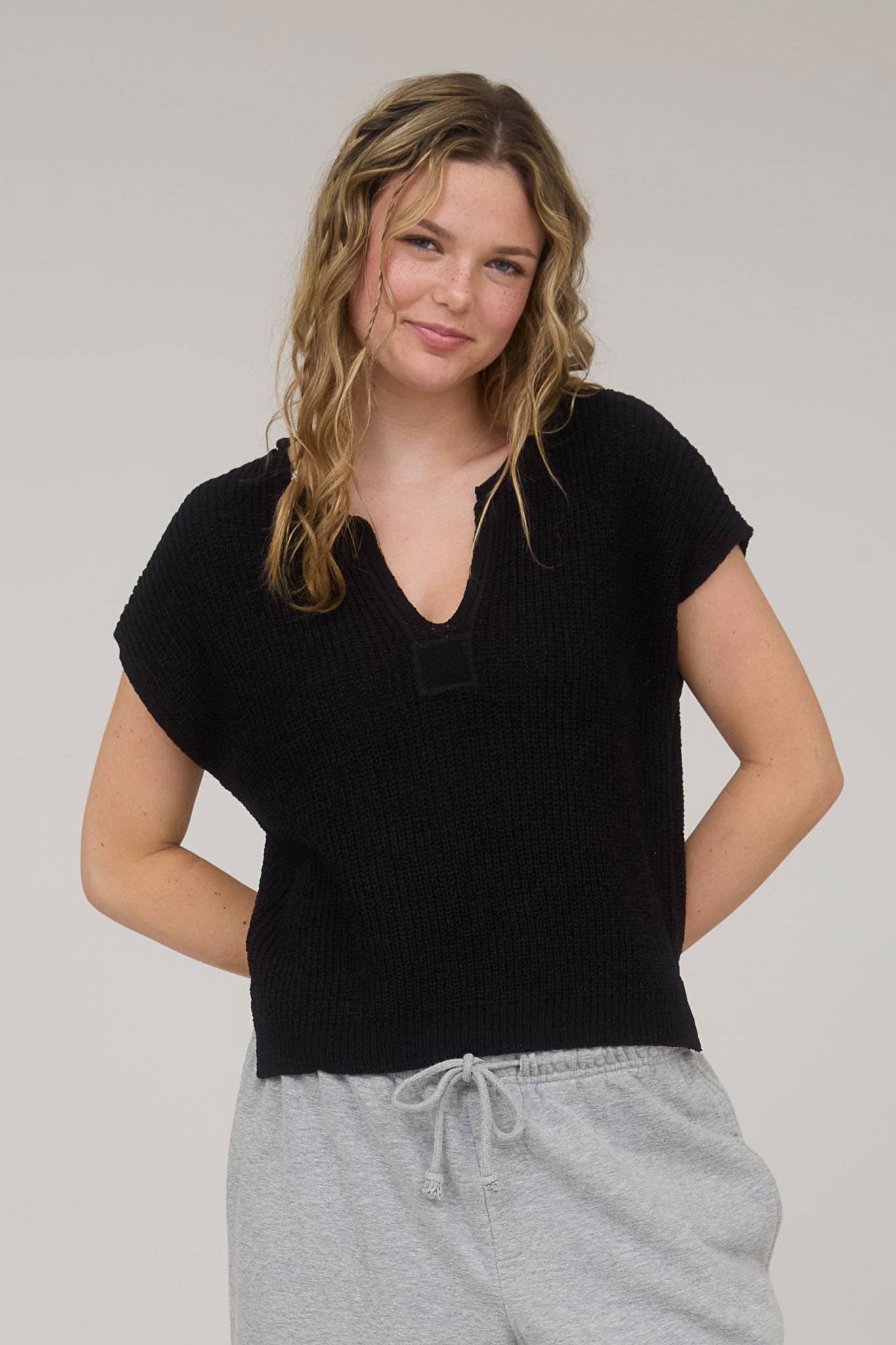 Woman wearing a black top and gray pants against a plain background