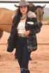 Woman in cowboy hat and patterned jacket standing next to a horse in an outdoor setting.