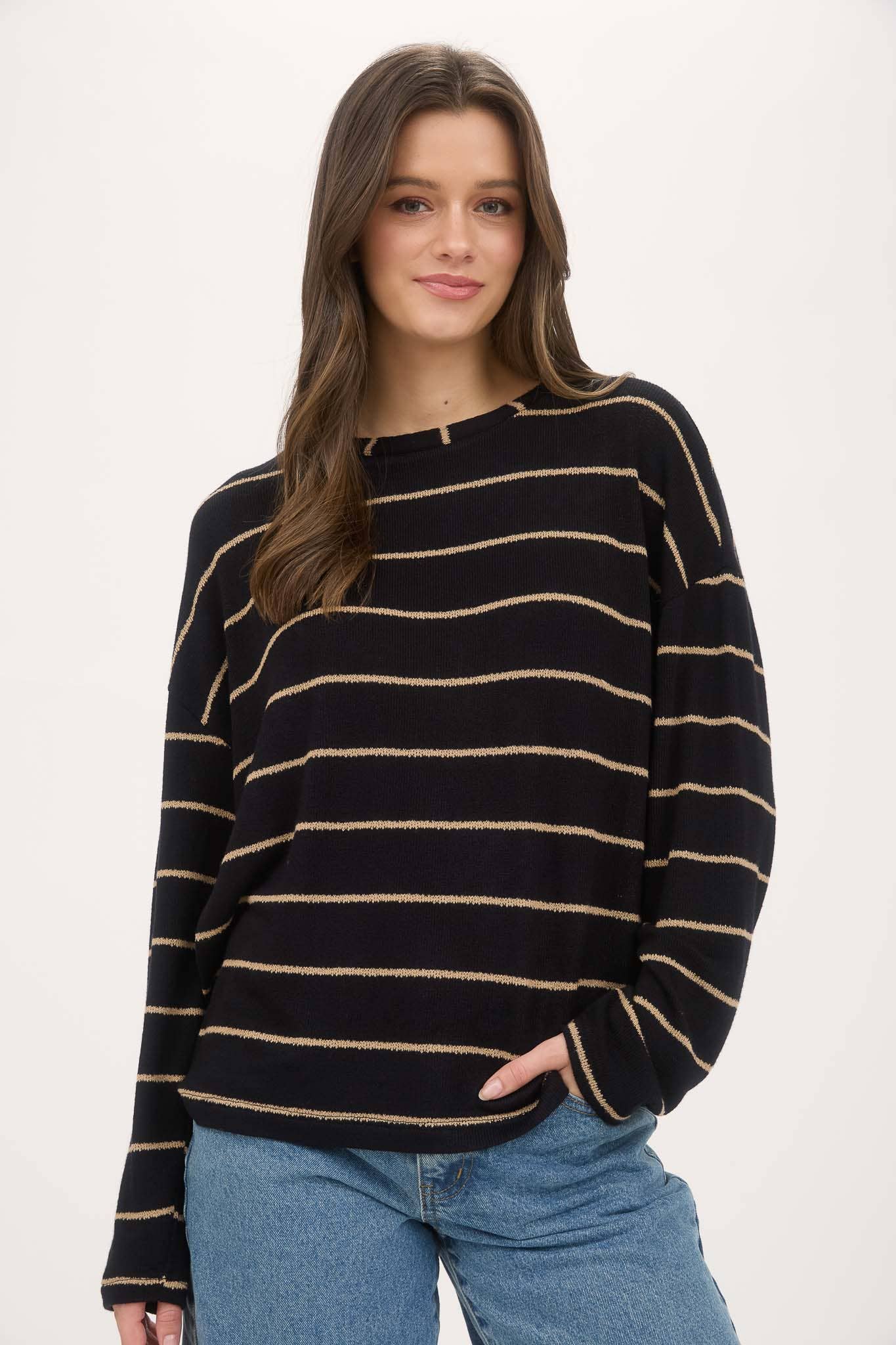 Woman wearing a black and gold striped sweater with blue jeans on a white background