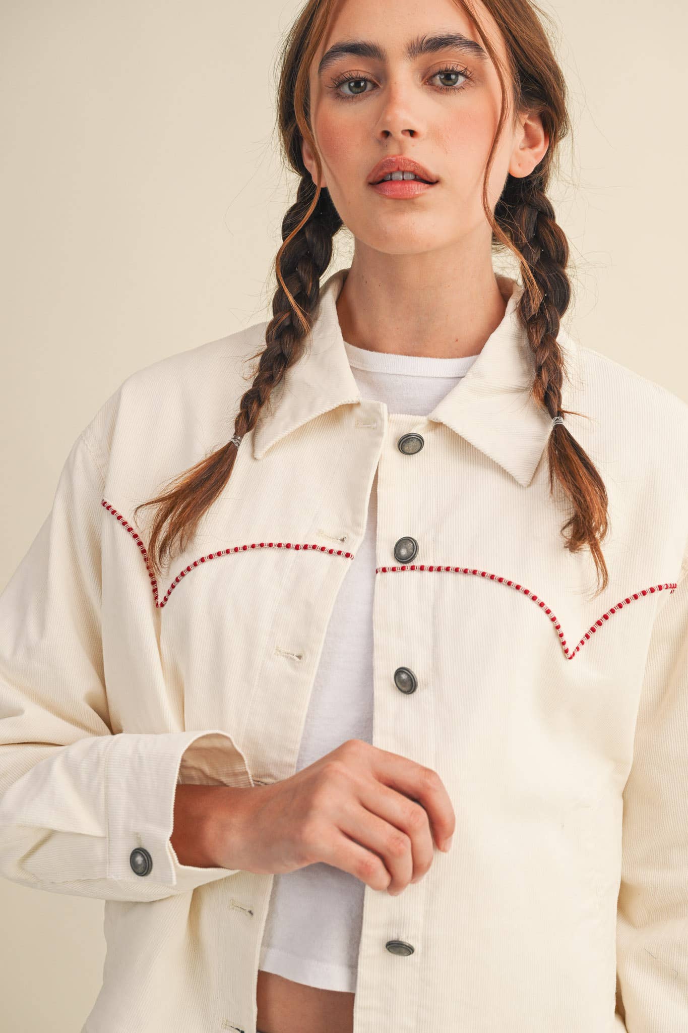 Woman wearing a cream-colored jacket with red stitching on a beige background