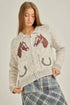 Woman wearing a knitted cardigan with horse and horseshoe patterns on a plain background