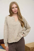 Woman wearing a beige sweater and brown pants against a plain background