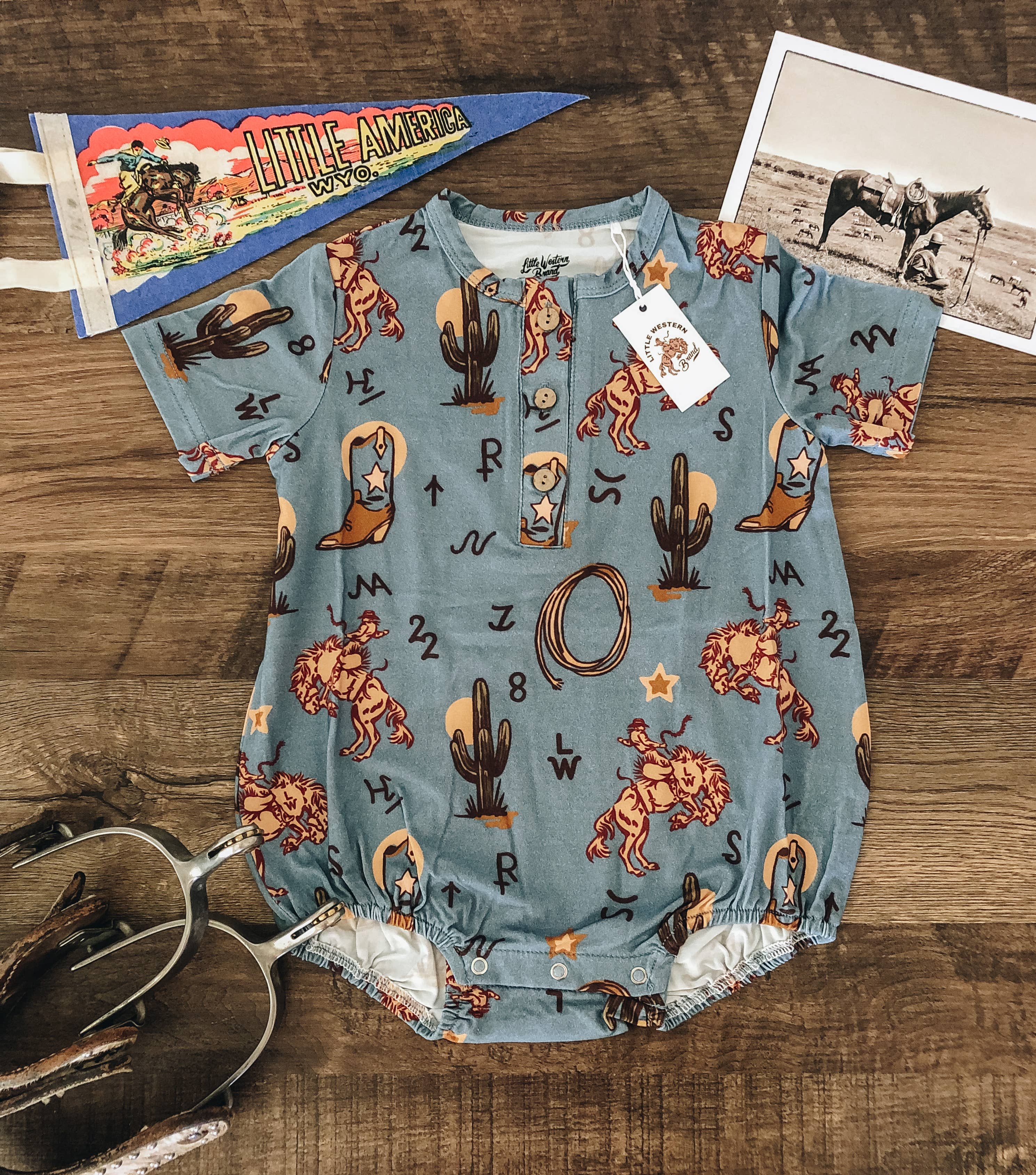 Baby western bamboo viscose bubble romper in vintage indigo blue with bronc, cactus, boot, and rope print, oversized fit with wood buttons and snap closure