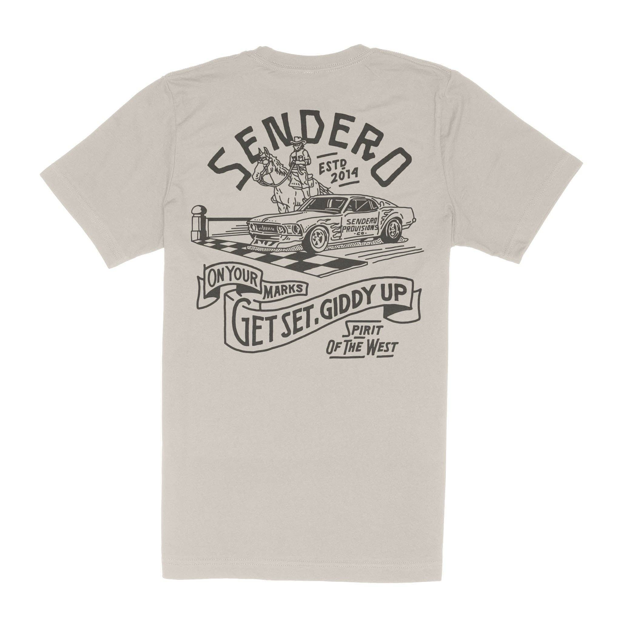Light brown t-shirt featuring a Sendero Provisions Co. graphic on the back with a cowboy on horseback next to a race car at a checkered starting line. The design includes the phrase "On Your Marks, Get Set, Giddy Up – Spirit of the West." Classic fit with a soft feel.