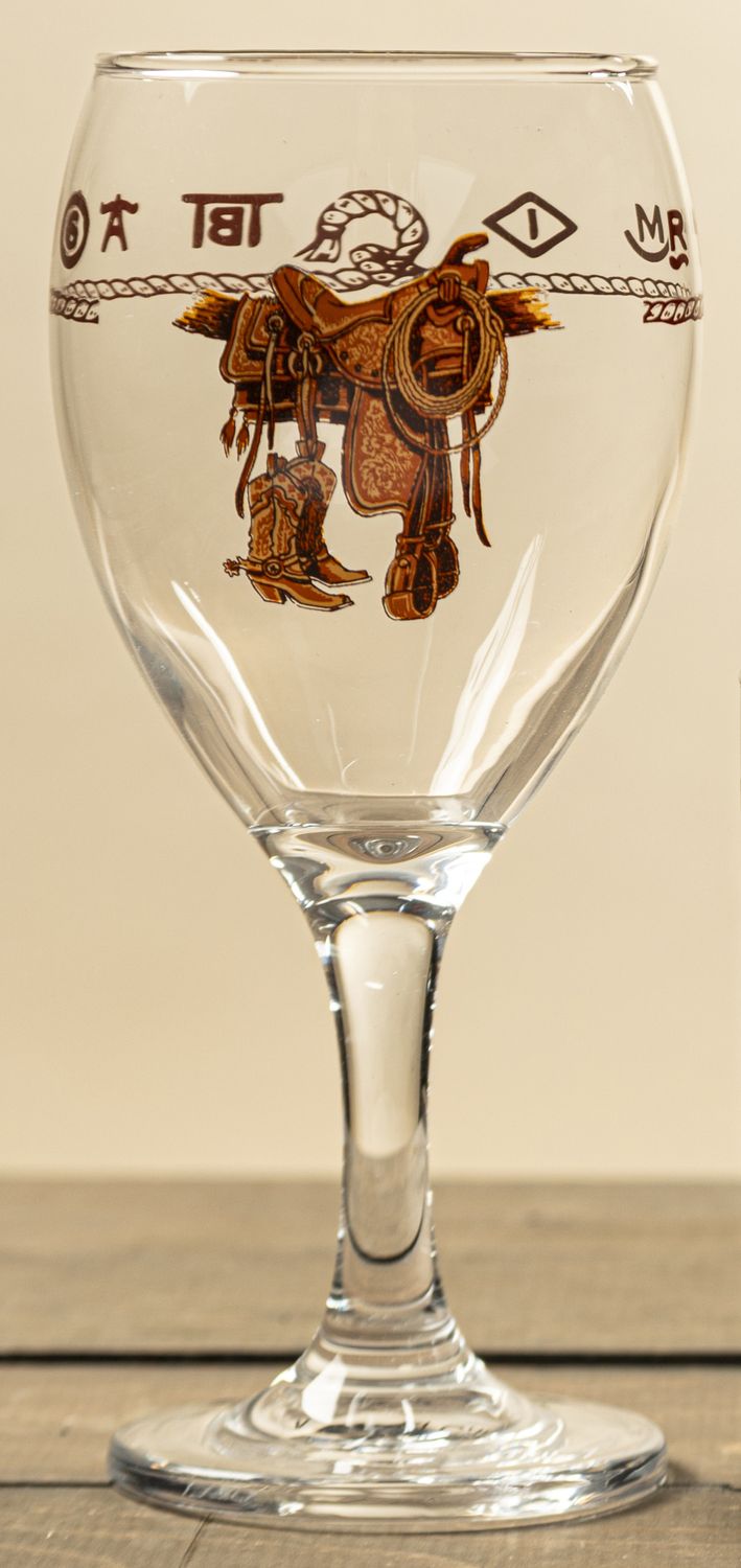 Set of four western-themed wine glasses featuring a dark brown imprint of boots and a saddle, surrounded by rope and livestock brand details. Dishwasher safe.