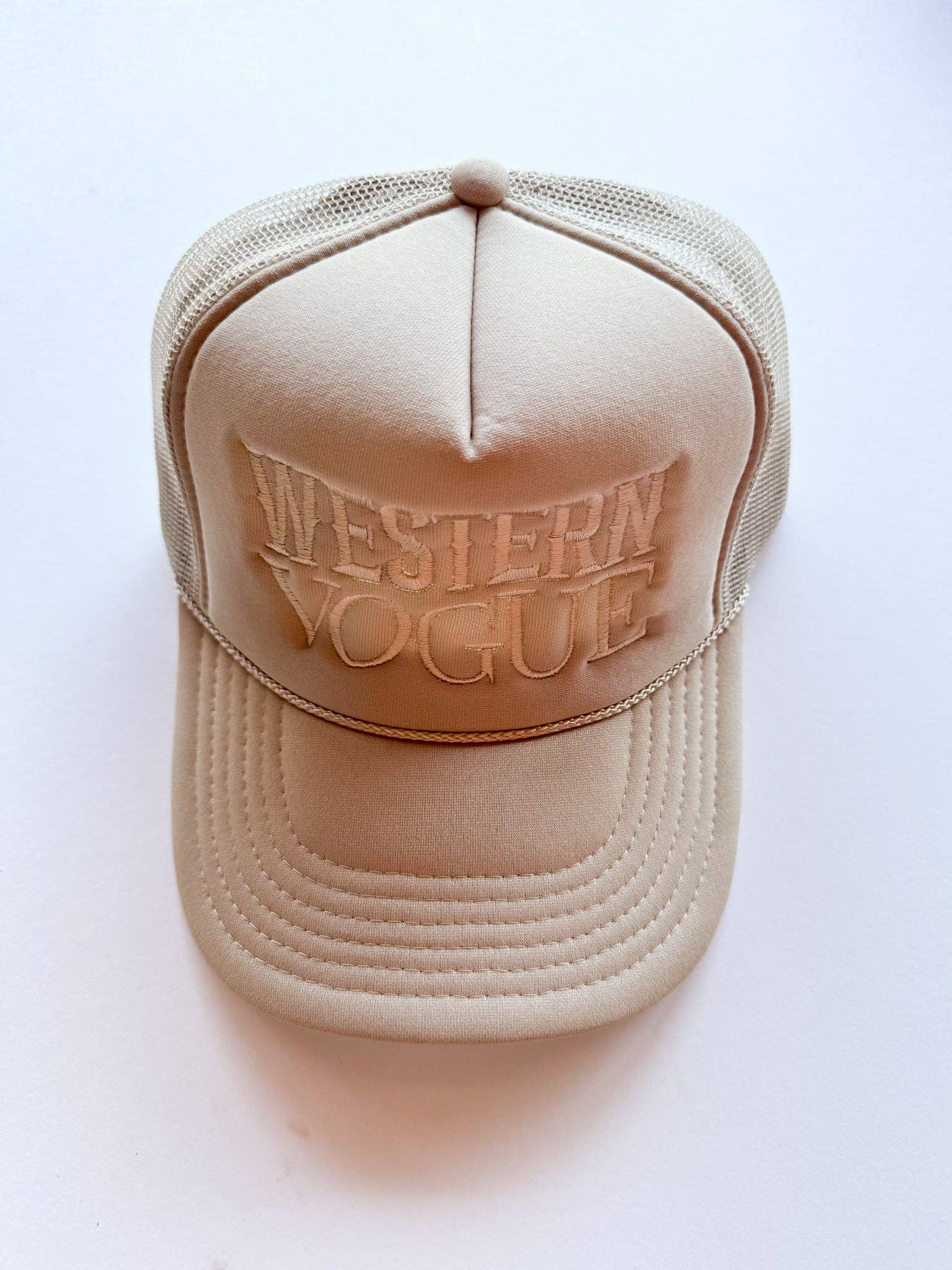 A monochromatic beige trucker hat with tonal puff embroidery reading "WESTERN VOGUE," a mesh back, and a classic rope detail across the brim. Stylish and modern with a Western edge.
