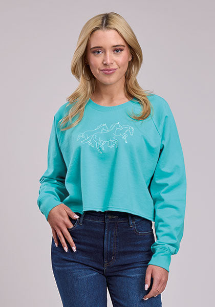 Women’s turquoise cropped fleece sweatshirt with running horses graphic, raglan long sleeves, scoop neckline, rib knit cuffs, raw hem, Roper western pullover top paired with dark denim jeans.