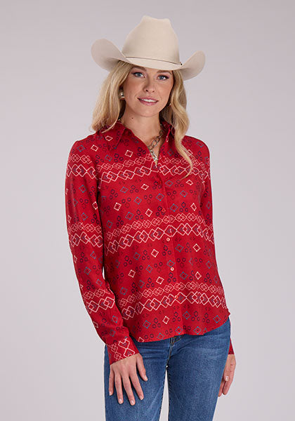 A woman wearing a red long sleeve shirt with a geometric "RWB Aztec" print, paired with blue jeans and accessorized with a beige cowboy hat.
