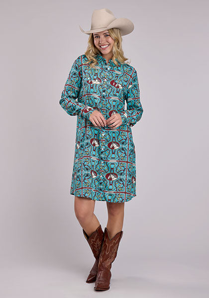 Woman wearing a turquoise scarf print Western shirt dress with long sleeves, button front, chest pockets, and cowboy boots, styled with a cream cowboy hat.