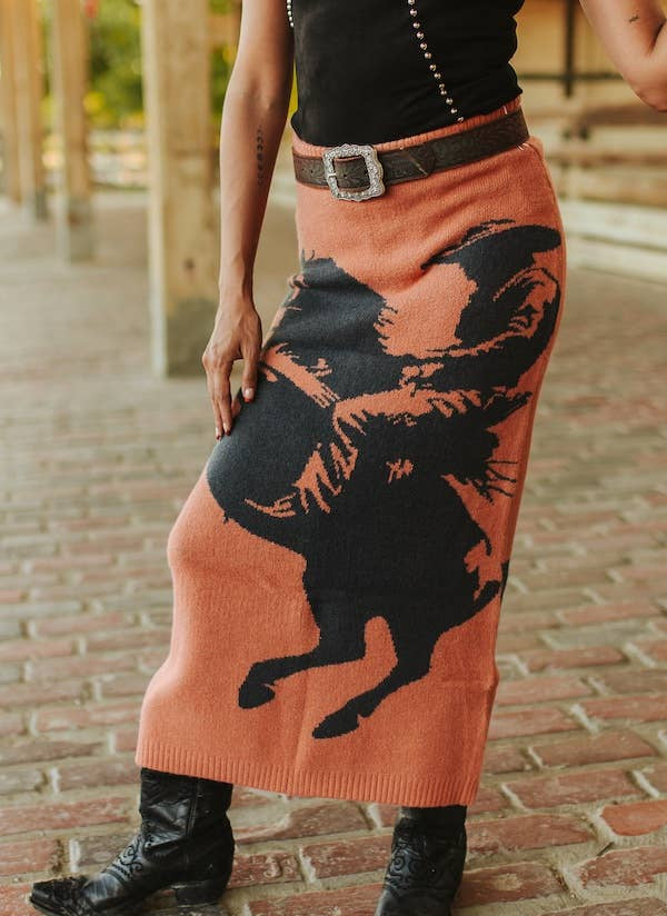 Person wearing a long, patterned skirt with a horse design on a brick surface.