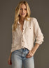 Woman wearing a beige button-up shirt and blue jeans against a gray background