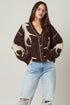 Woman wearing a brown cardigan with abstract patterns and light blue jeans on a plain background