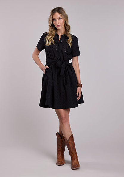 Woman wearing a black Stetson cotton eyelet Western shirt dress with short sleeves, button front, elastic waist, tie belt, and cowboy boots.