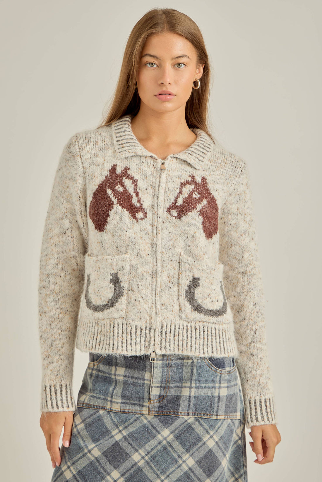 Woman wearing a knitted cardigan with horse designs on a plain background