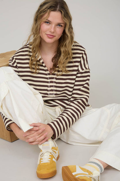 Woman wearing a striped shirt and white pants sitting on a white floor.