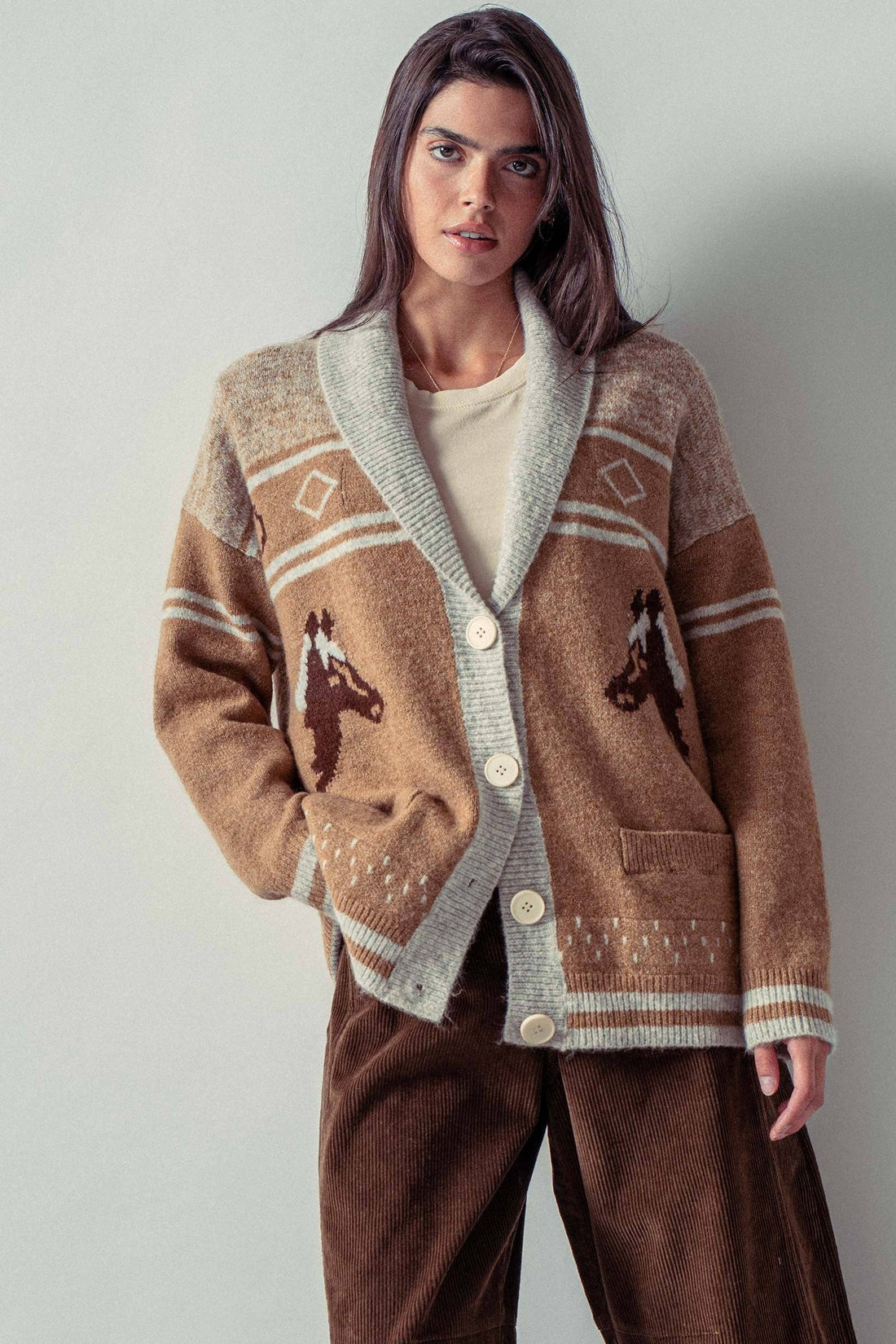 Woman wearing a brown cardigan with horse designs on a plain background