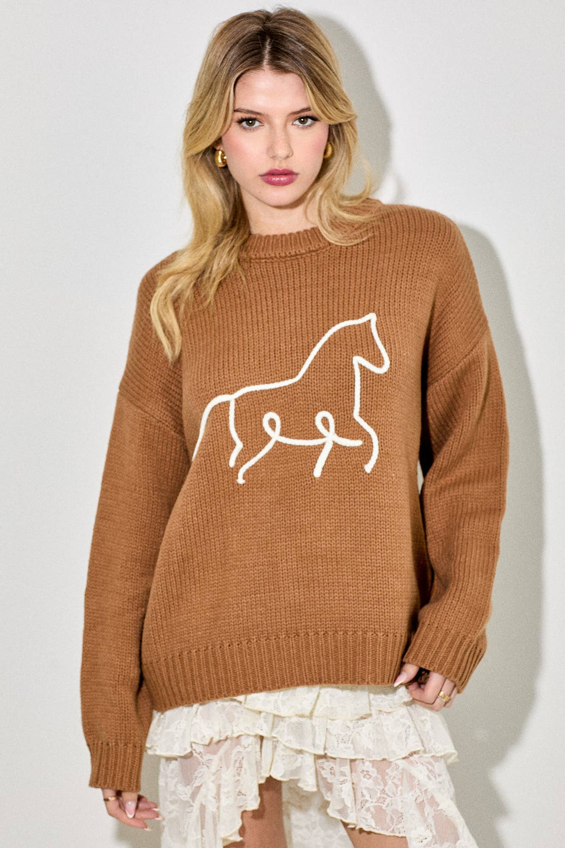 Woman wearing a brown sweater with a horse design against a white background