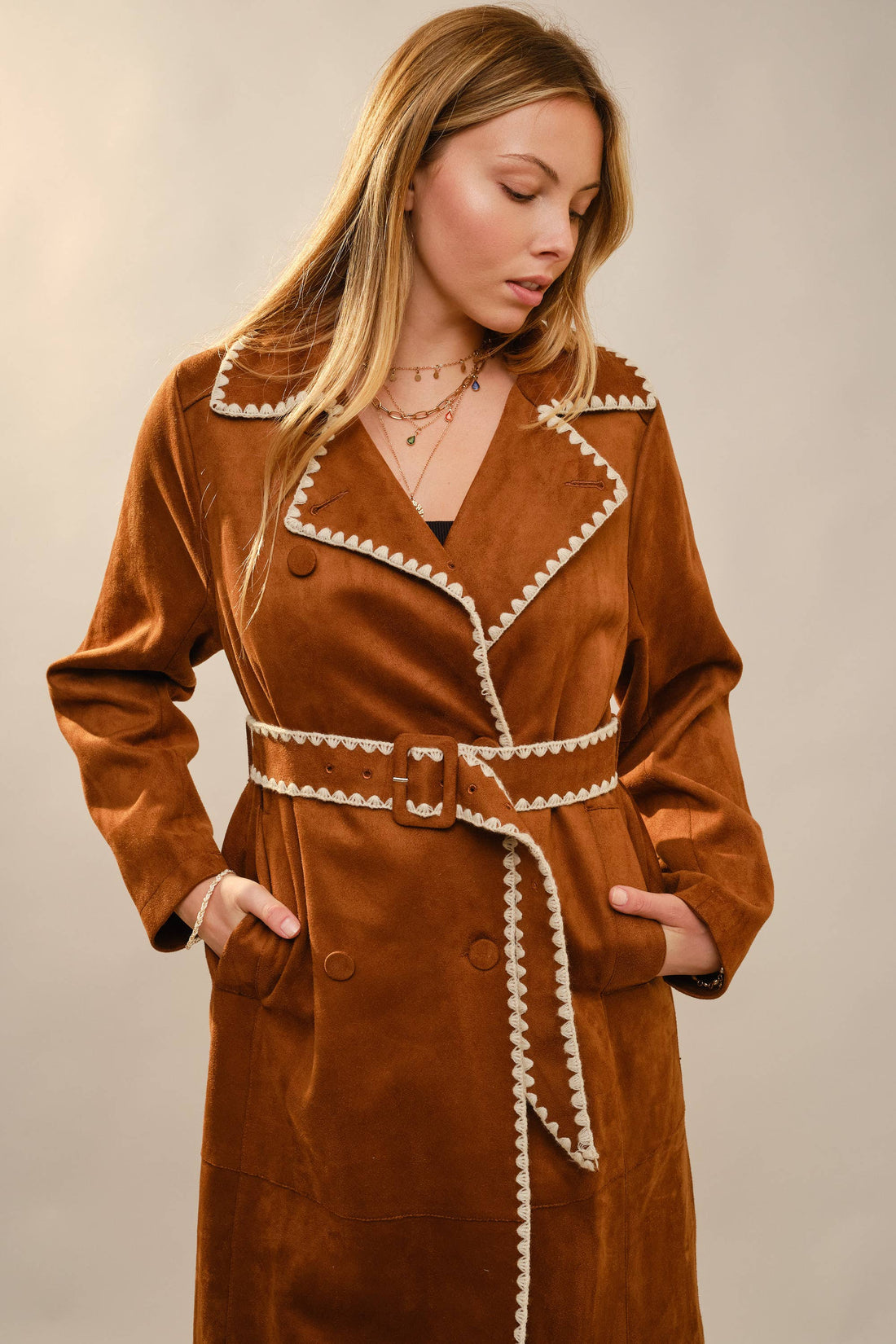 Woman wearing a brown coat with white trim against a plain background