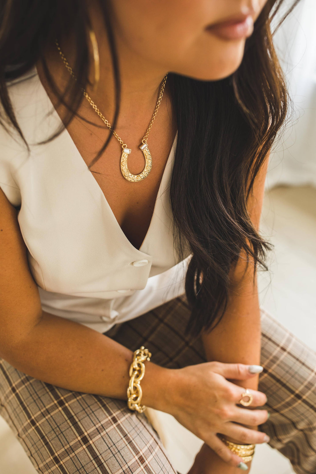 Woman wearing gold jewelry including a necklace, bracelet, and ring.