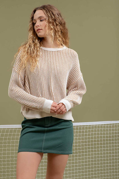 Woman wearing a beige sweater and green skirt standing on a tennis court.