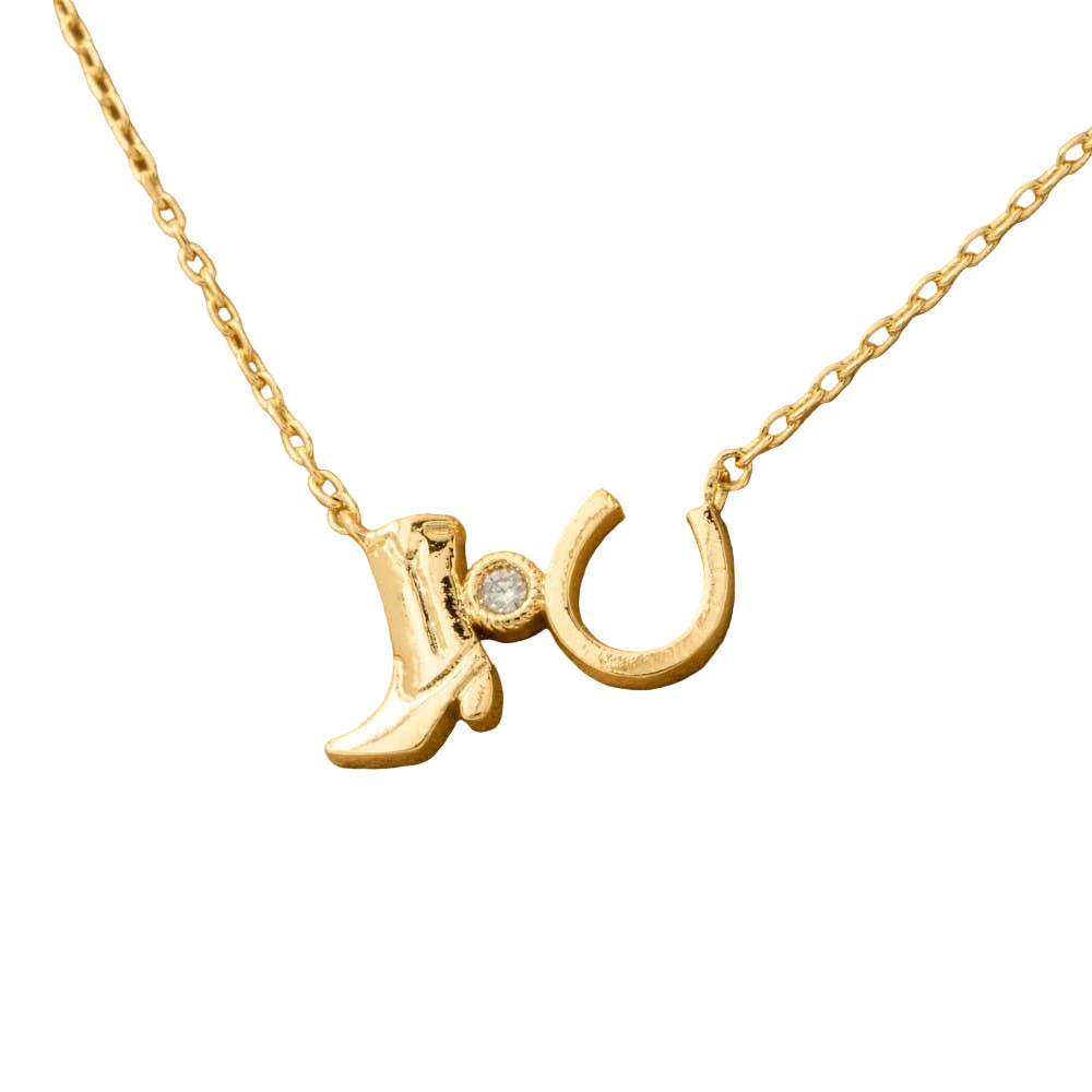 Gold necklace with boot and horseshoe pendant on a beige background