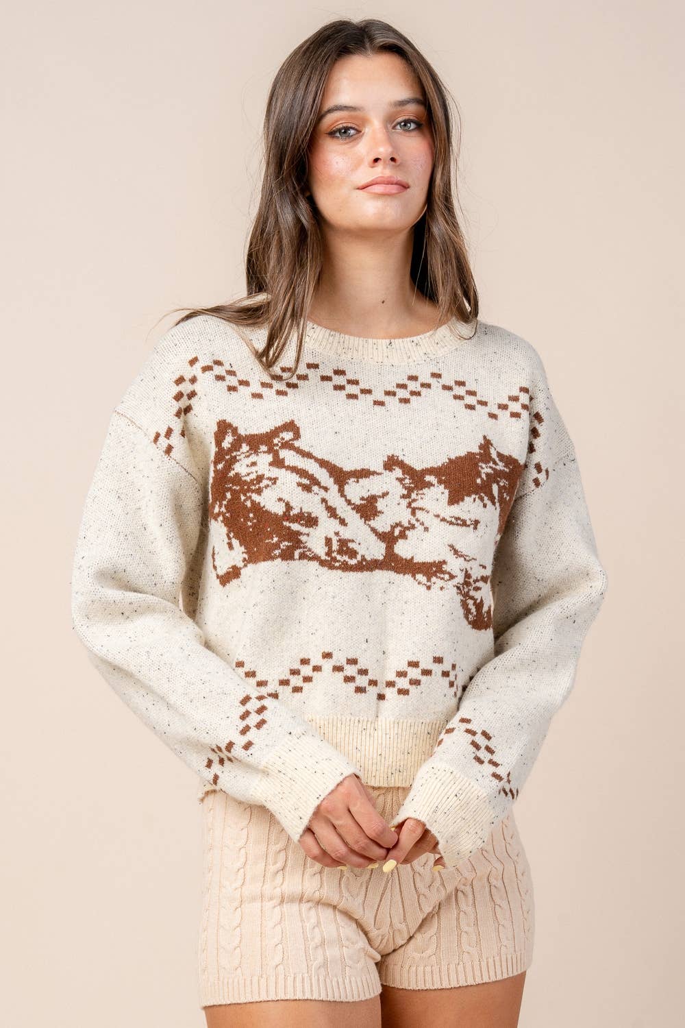 Woman wearing a cream sweater with brown pattern on a beige background