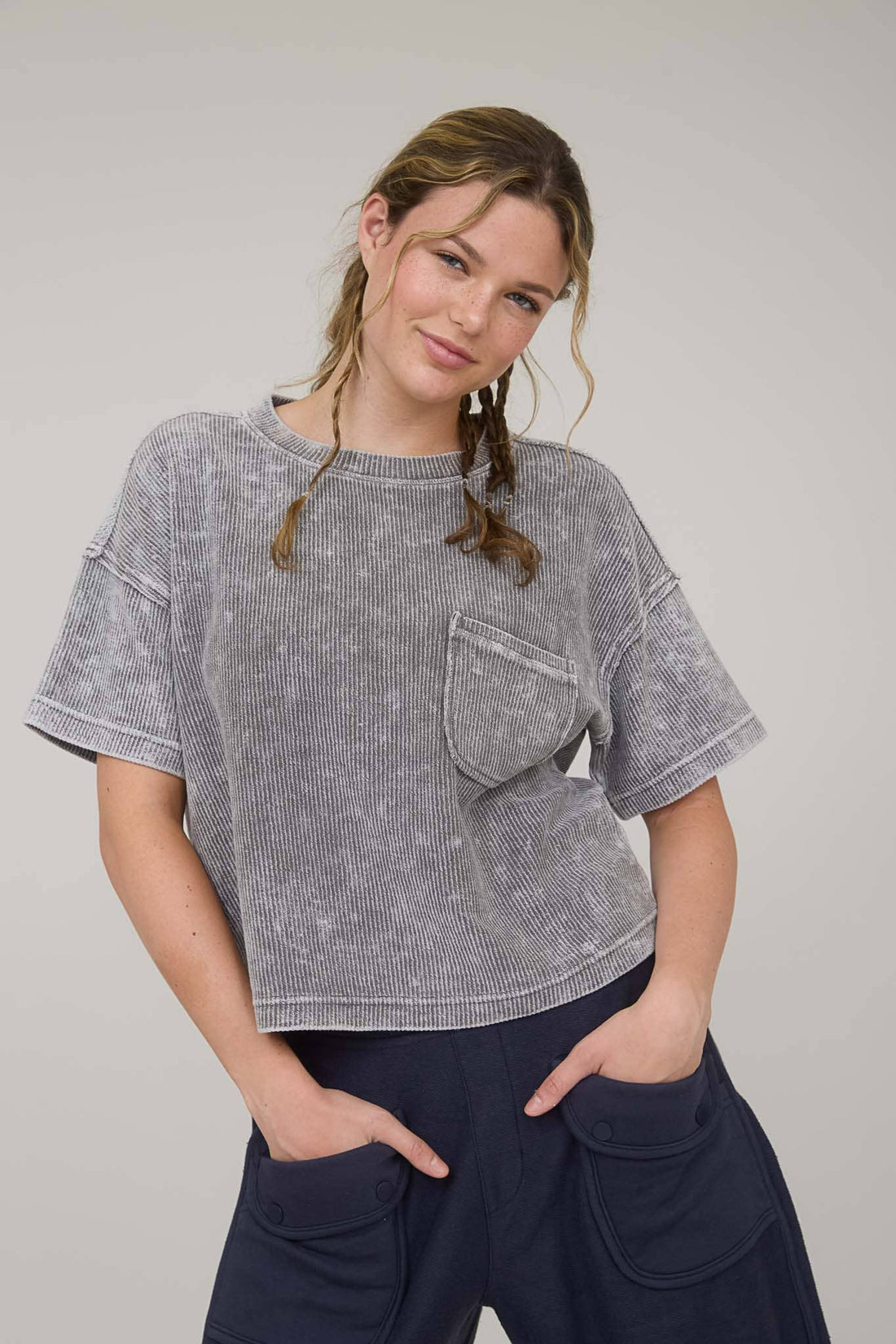 Woman wearing a gray patterned top with a pocket on a plain background
