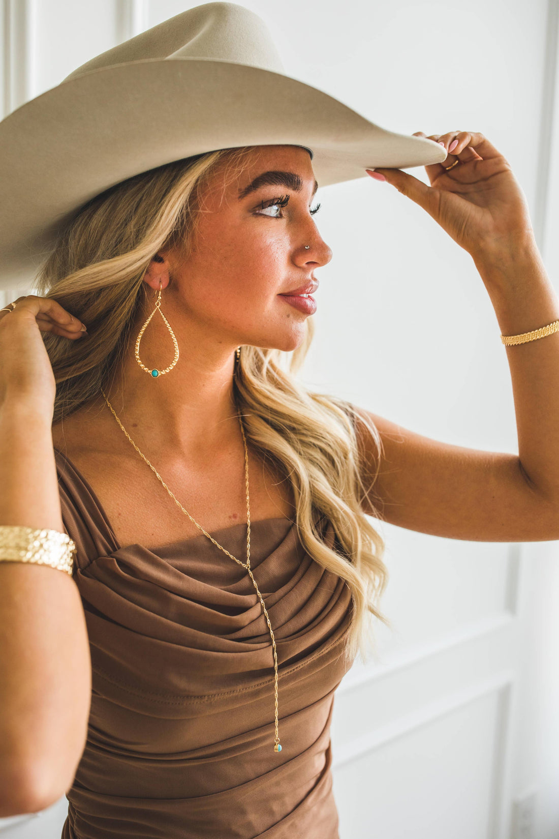 Woman wearing a beige hat and dress, holding the hat with one hand.