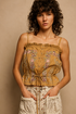 Model wearing the Golden Mesa Tank, a golden tan sleeveless poplin top featuring floral embroidery, decorative trim, button-front closure, adjustable front tie, and a softly gathered waist, paired with a cream floral skirt.