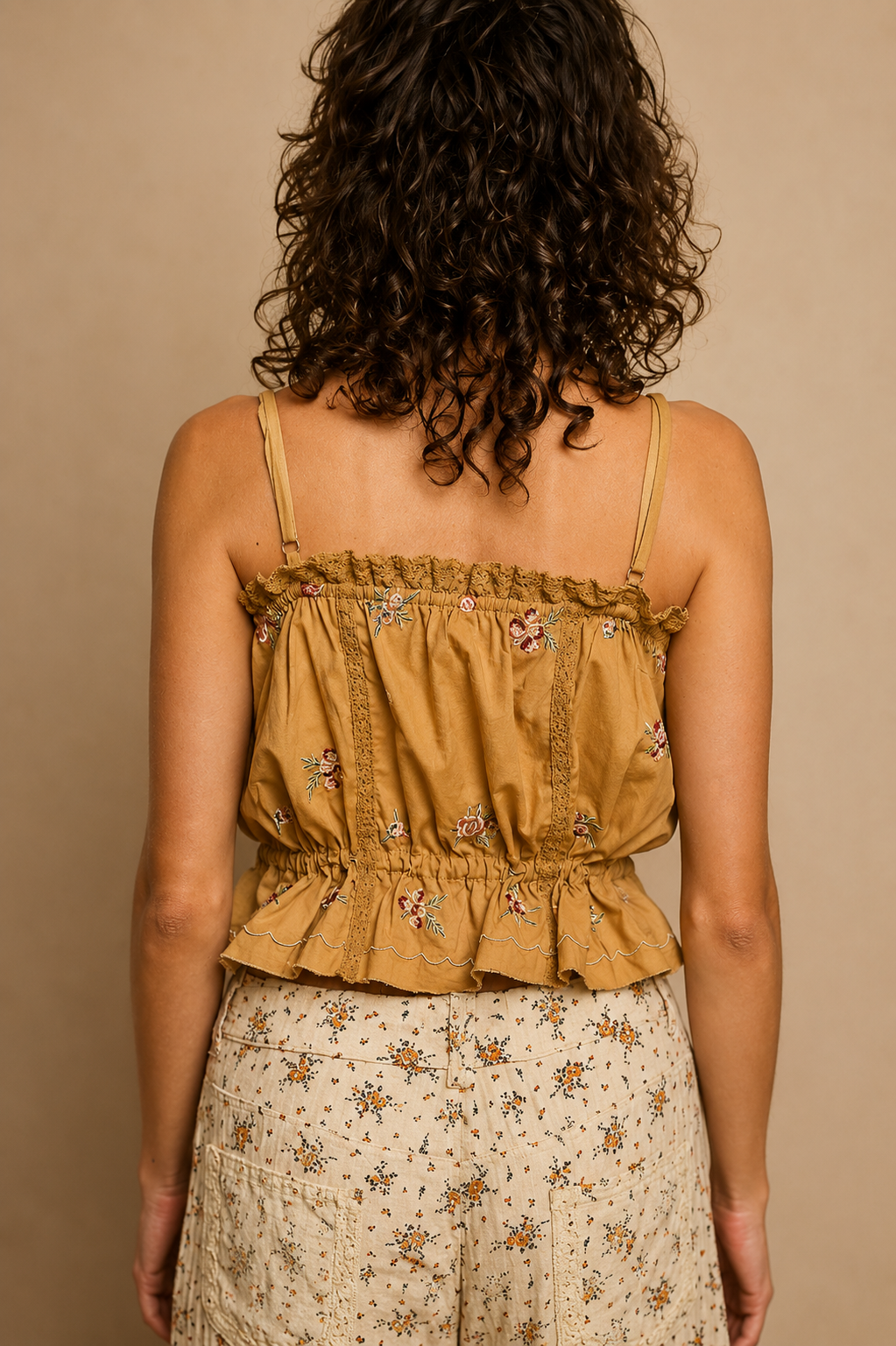Model wearing the Golden Mesa Tank, a golden tan sleeveless poplin top featuring floral embroidery, decorative trim, button-front closure, adjustable front tie, and a softly gathered waist, paired with a cream floral skirt.
