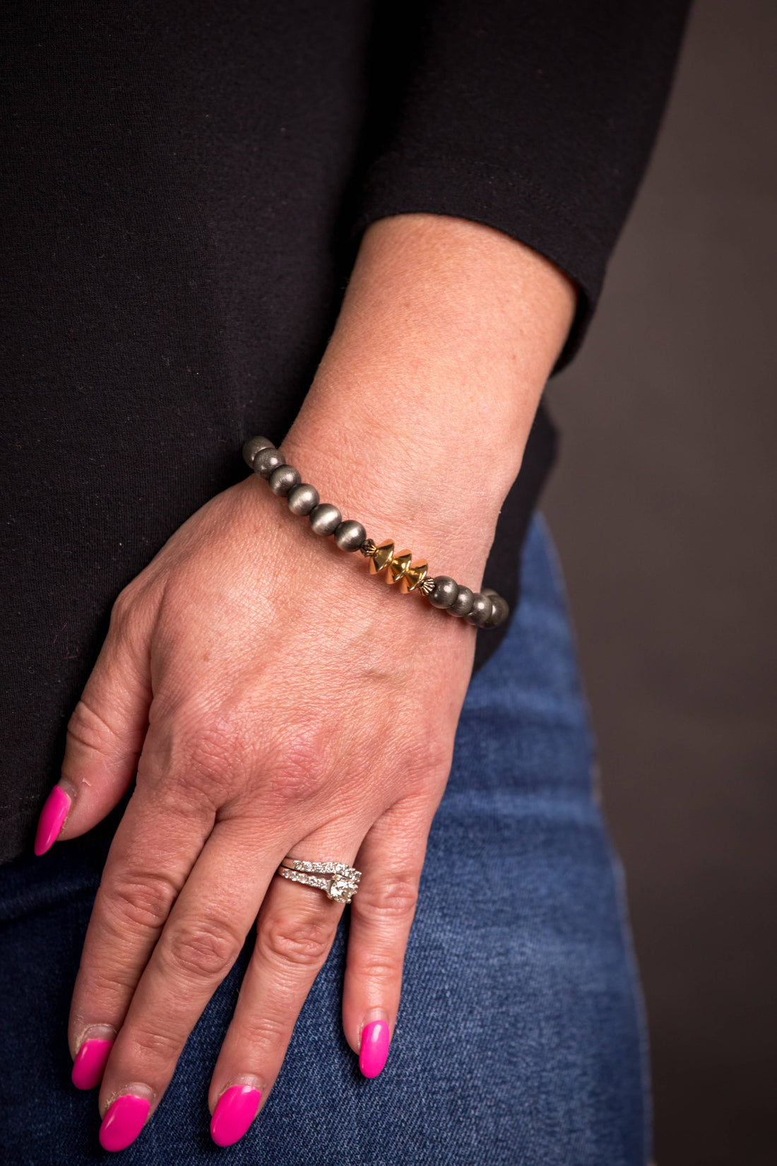 Hand wearing a bracelet and ring with pink nail polish on a dark background