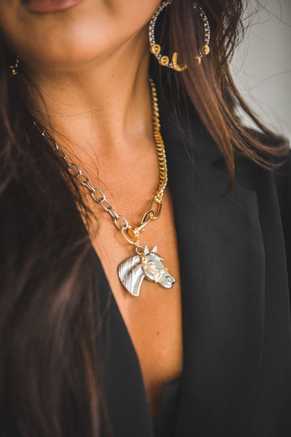 Close-up of a person wearing a gold necklace with a horse head pendant.