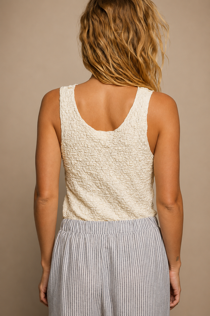 Model wearing the Ivory Heirloom Tank, a cream sleeveless scoop-neck top featuring floral lace panels, textured mixed fabrics, exposed seam detailing, and a relaxed fit, paired with blue and ivory striped pants.