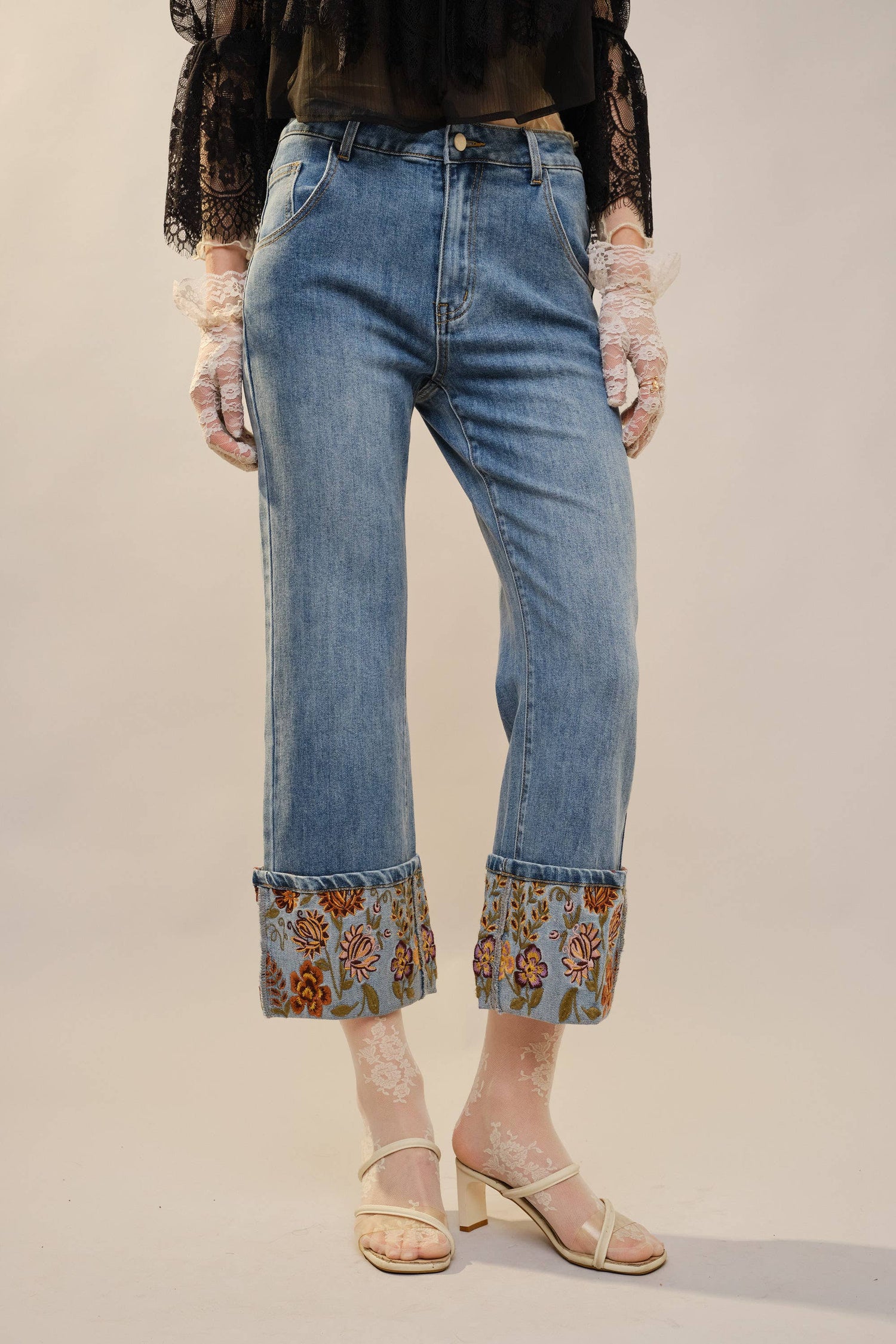 Person wearing blue jeans with floral cuffs on a plain background