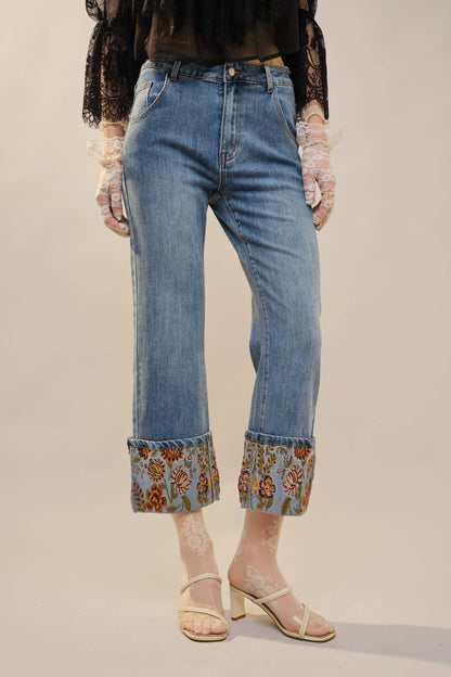 Person wearing blue jeans with floral cuffs on a plain background