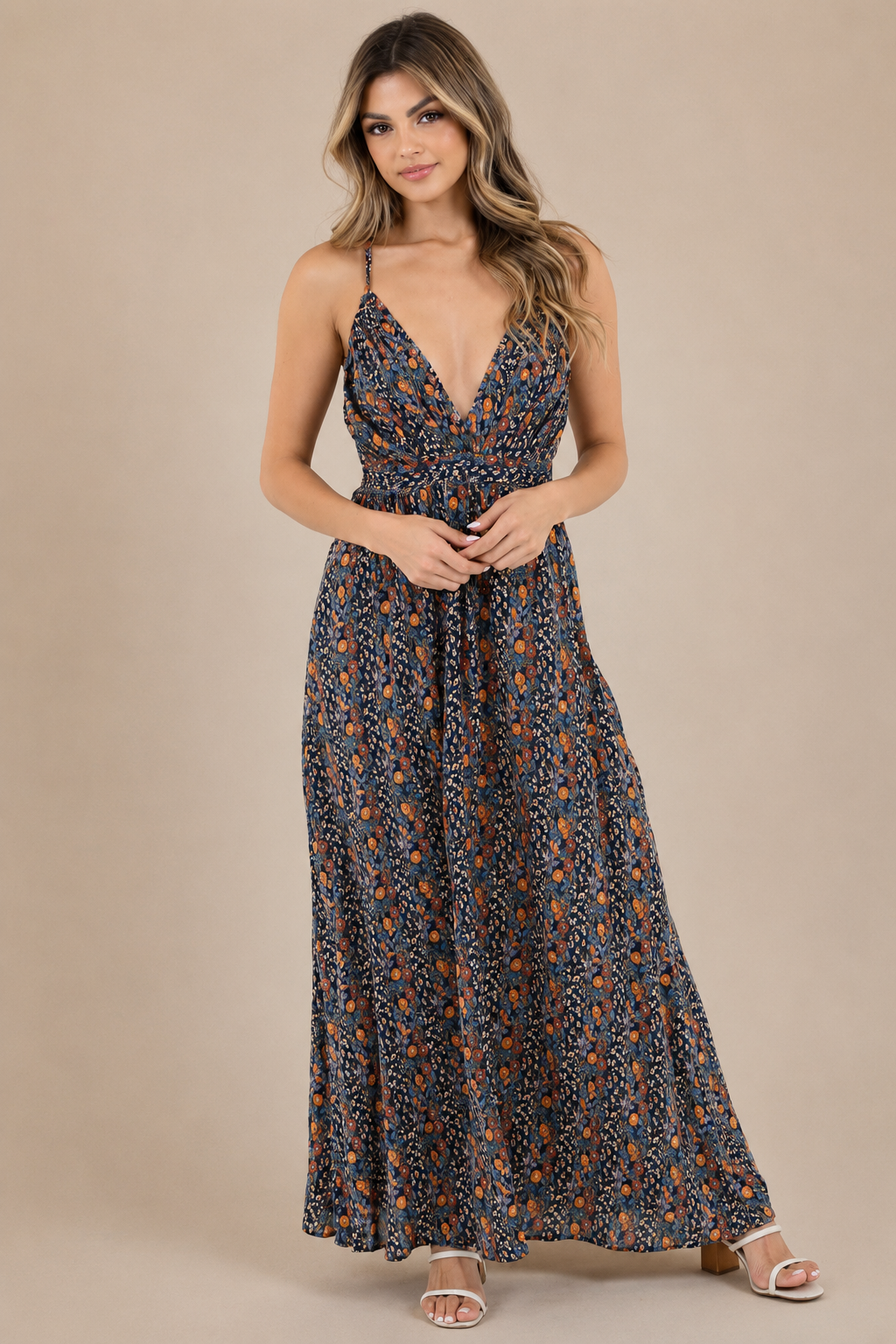 Model wearing the Midnight Meadow Maxi Dress, a navy floral print maxi dress with a surplice V-neckline, adjustable spaghetti straps, a gathered empire waist, and a flowing full-length skirt, paired with white heeled sandals.