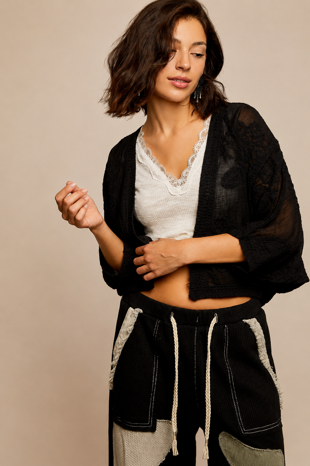 Model wearing the Noir Canyon Kimono, a lightweight black open-front cardigan featuring a textured crochet-inspired design, relaxed fit, and three-quarter sleeves, layered over a cream lace-trim camisole and patchwork lounge pants.