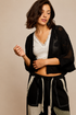 Model wearing the Noir Canyon Kimono, a lightweight black open-front cardigan featuring a textured crochet-inspired design, relaxed fit, and three-quarter sleeves, layered over a cream lace-trim camisole and patchwork lounge pants.