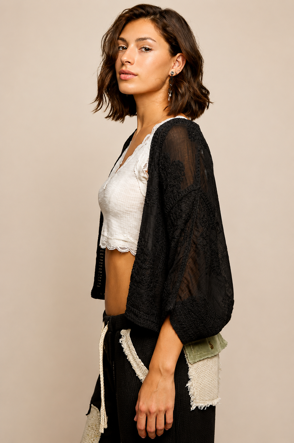 Model wearing the Noir Canyon Kimono, a lightweight black open-front cardigan featuring a textured crochet-inspired design, relaxed fit, and three-quarter sleeves, layered over a cream lace-trim camisole and patchwork lounge pants.