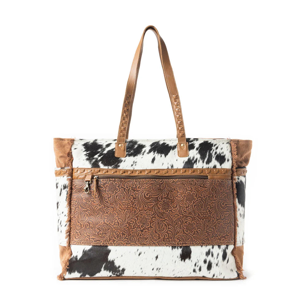 S-10917 Cowhide Tooled Leather Tote featuring a genuine hair-on hide body, intricate floral tooled leather panel, sturdy leather handles with rivet details, and a spacious design with exterior and interior pockets for functionality and style.