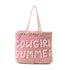 S-11764 Cowgirl Summer Tote featuring a handwoven rug and canvas design with "COWGIRL SUMMER" spelled in cowrie shells. Spacious with a vibrant pink lining, sturdy handles, and interior pockets for storage.