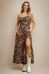 Model wearing the Saguaro Sky Maxi Dress, a Southwestern-inspired cactus print maxi dress with adjustable spaghetti straps, a fitted bodice, hidden side pockets, a thigh-high side slit, and white cowboy boots.